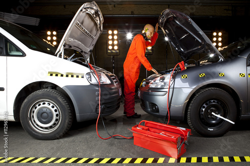 A crash test dummy using jumper cables with two cars photo