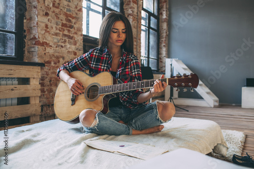 Young woman playing guitar while sitting on bed at home photo