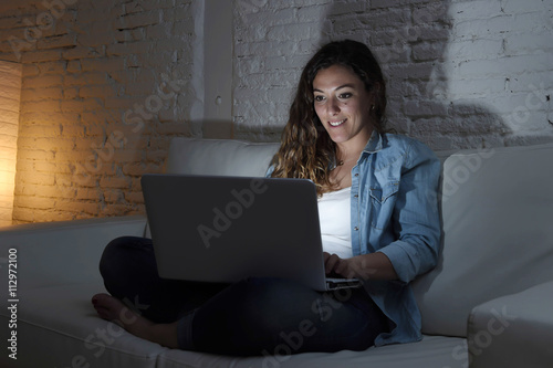 attractive relaxed woman at home sitting happy on couch using laptop at night