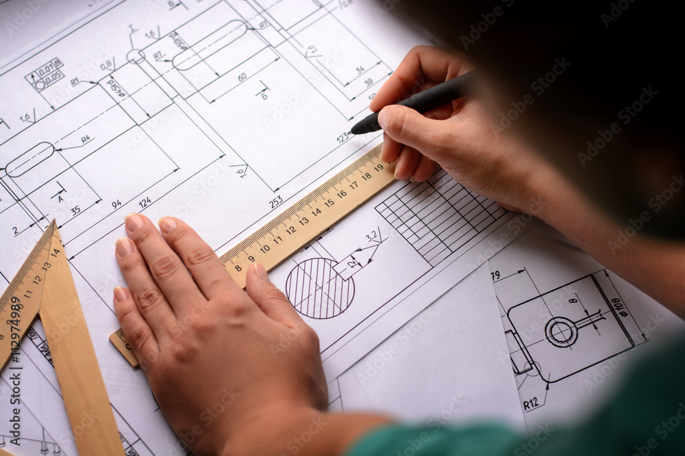 Girl architect draws a plan, graph, design, geometric shapes by pencil on large sheet of paper at office desk. Soft focus Girl architect draws a plan, graph, design, geometric shapes by pencil on large sheet of paper at office desk. Soft focus