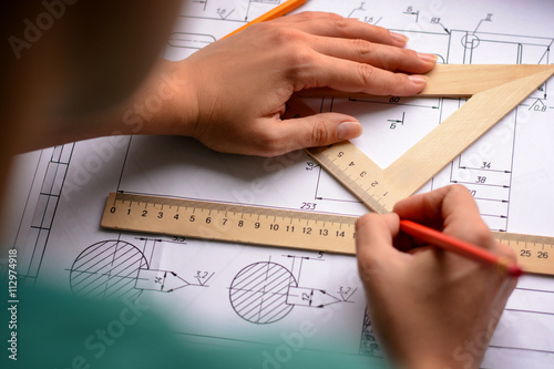 Girl architect draws a plan, graph, design, geometric shapes by pencil on large sheet of paper at office desk. Soft focus
