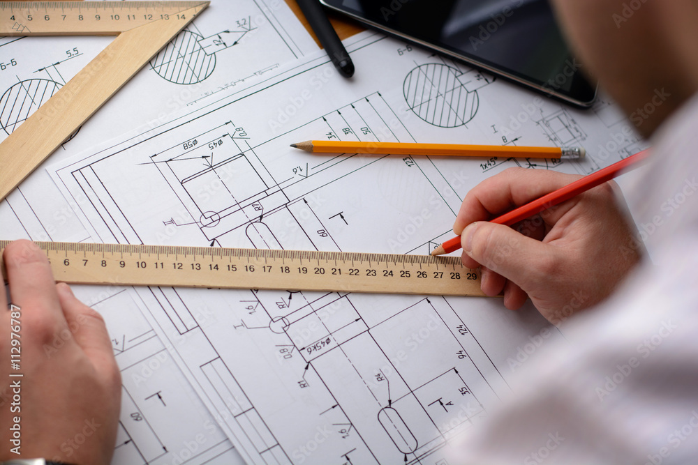 Man architect draws a plan, graph, design, geometric shapes by pencil on large sheet of paper at office desk Man architect draws a plan, graph, design, geometric shapes by pencil on large sheet of paper at office desk