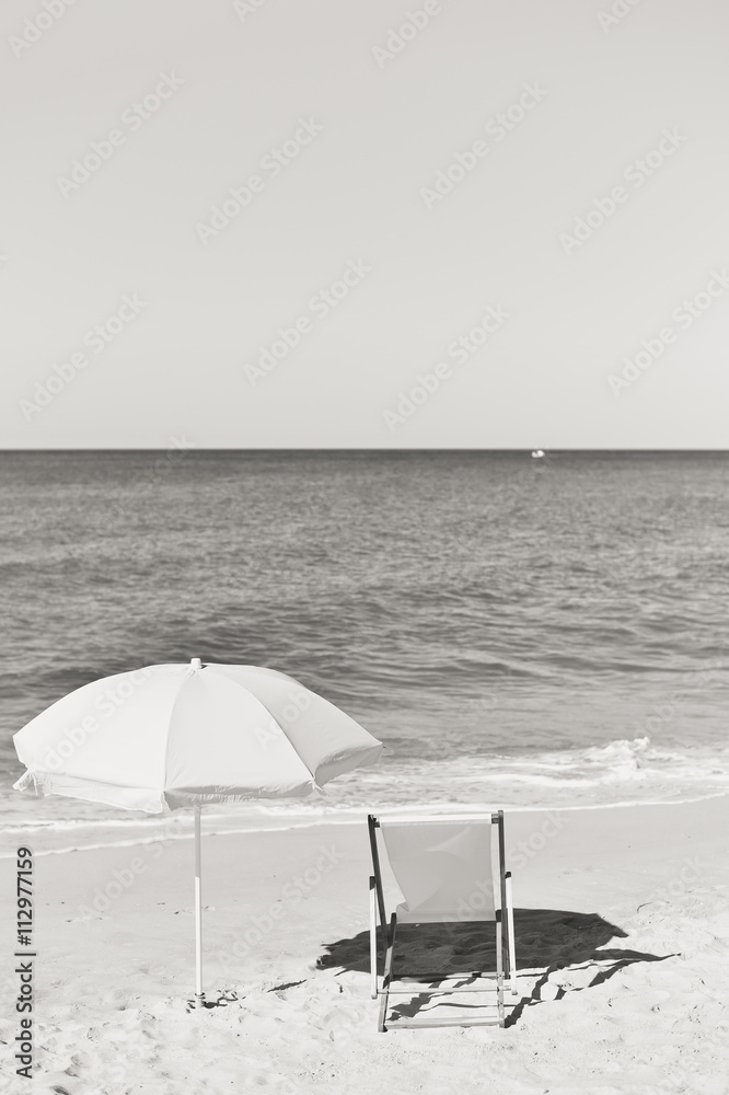 Black white photo of umbrella and wooden chair on Atlantic sandy beach