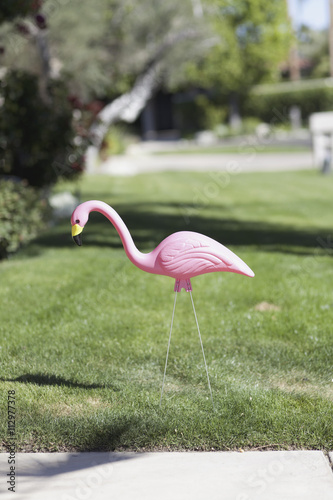 A plastic pink flamingo stuck in a lawn, close-up photo