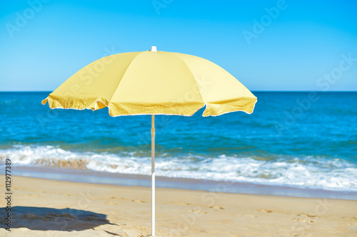 Yellow parasol on desert ocean beach over blue sky