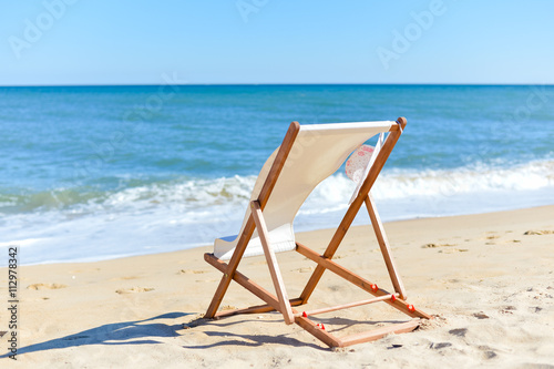 Back View Of Woman's Hat and Deckchair On Sandy Beach