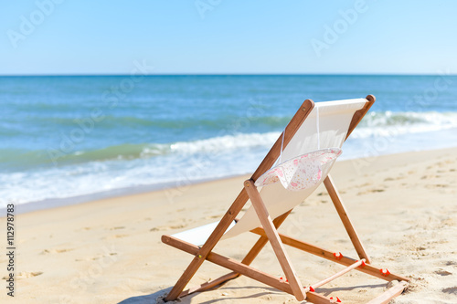 Fototapeta Naklejka Na Ścianę i Meble -  Back View Of Woman's Hat and Deckchair On Sandy Beach