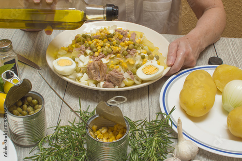 persona vertiendo aceite de oliva sobre las patatas,  preparando patatas cocidas, elaborando un plato con todos los ingredientes, ingredientes sobre la mesa