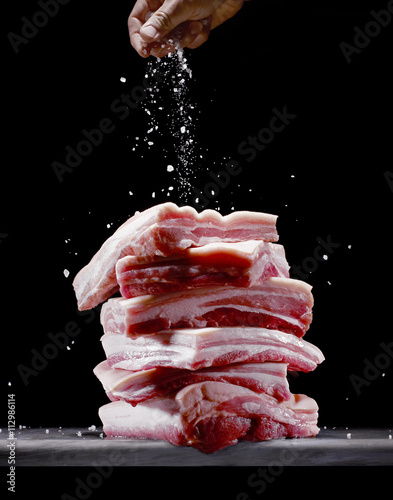 Person sprinkling salt onto pork belly photo