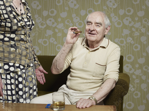 Senior man sitting on couch smoking cigar