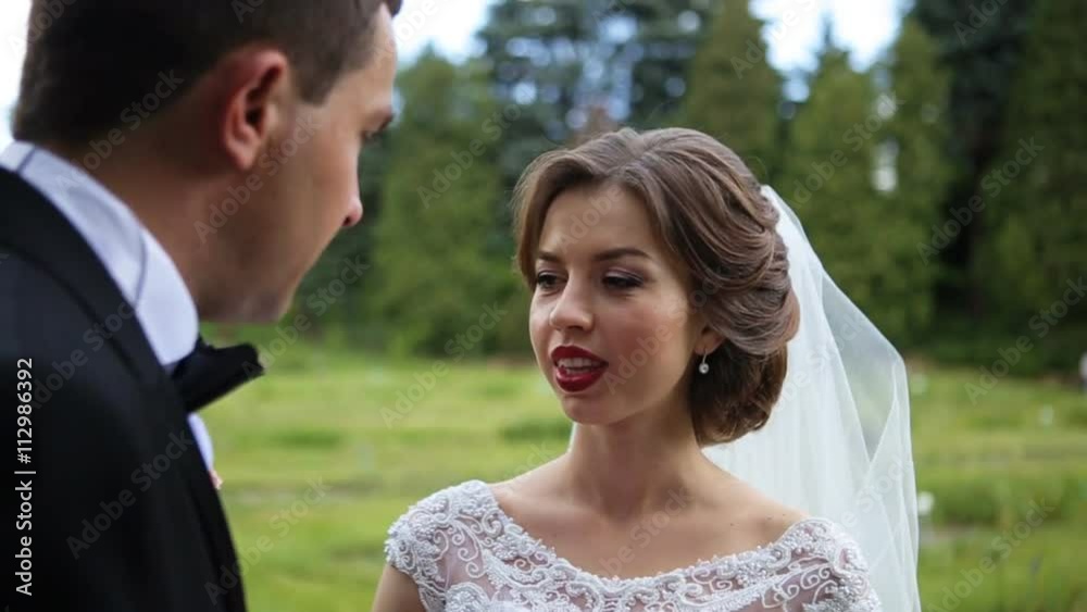 Beautiful happy brunette bride with red lips telling something to her groom standing back to the camera Beautiful happy brunette bride with red lips telling something to her groom standing back to the camera