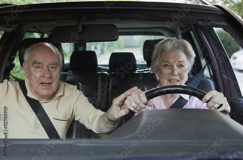 Woman has trouble driving while man in passenger tries to guide her hand photo