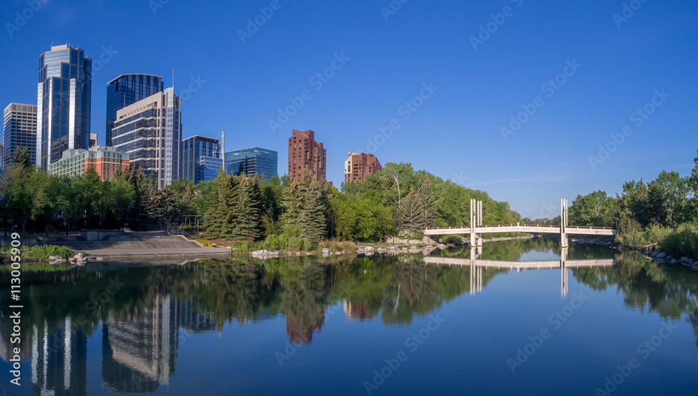 Foot bridge reflected in the Bow River at princes island park and the urban skyline in Calgary Alberta.