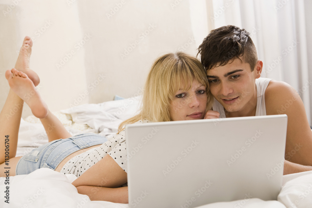 A young couple lying on a bed using a laptop A young couple lying on a bed using a laptop