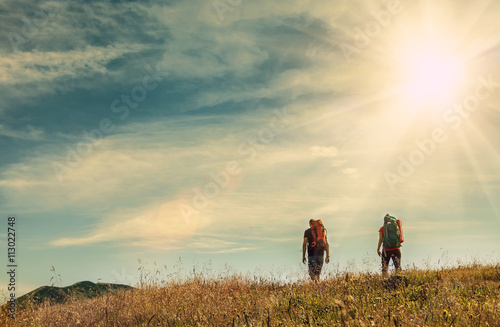 Two mountain travelers with backpacks under blue sky © Soloviova Liudmyla