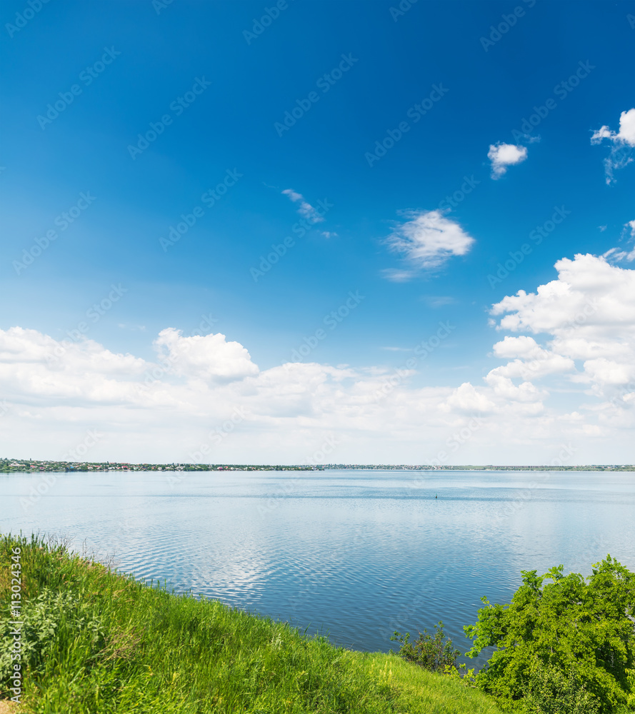 deep blue sky with clouds over river and green grass