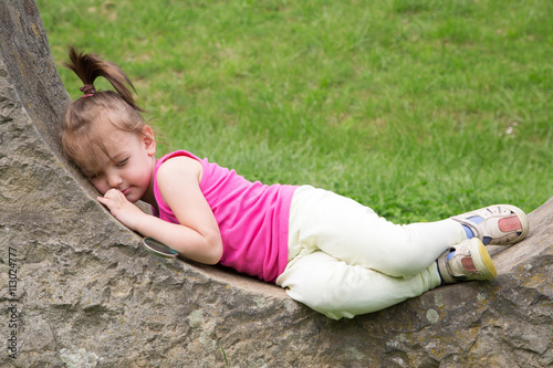 Sleepy Little Girl Resting On The Stonewall In The Park