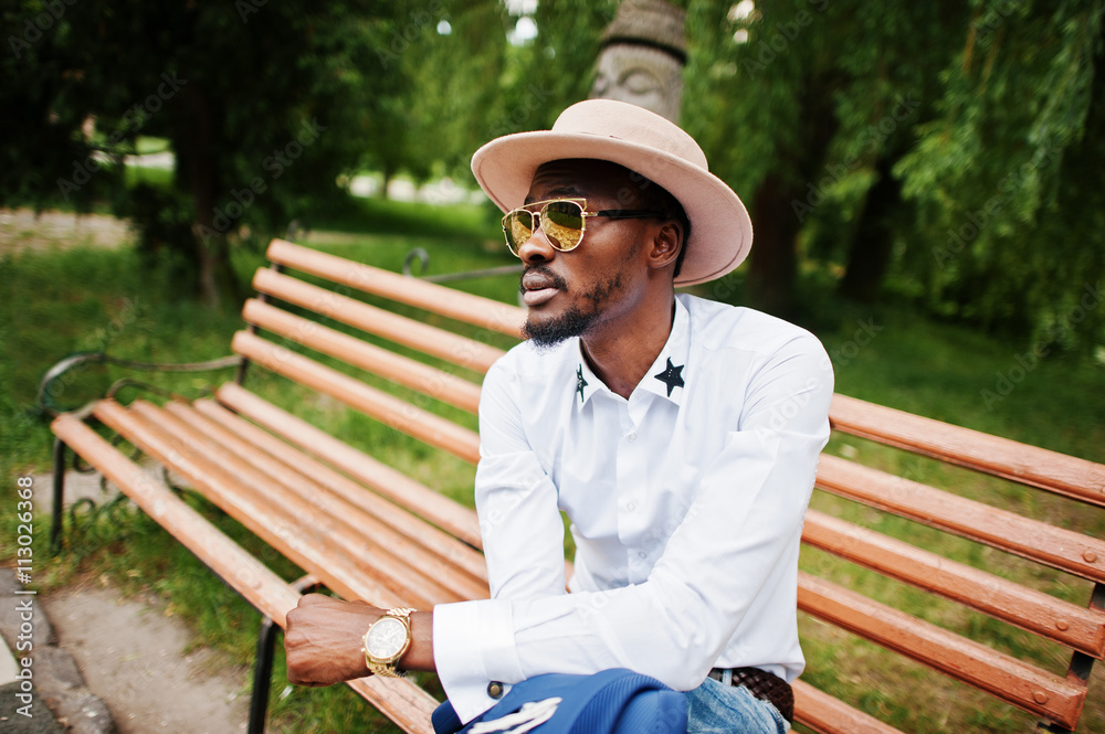 Rich black man sitting on bench at golden sunglasses and hat Rich black man sitting on bench at golden sunglasses and hat