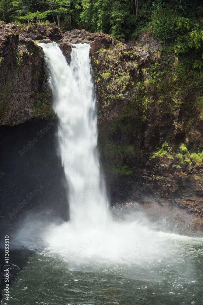 Fototapeta premium Rainbow Falls rushes into a large pool. The waterfall flows over a lava cave
