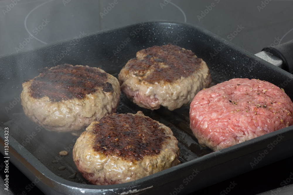 raw burgers, beef in a frying pan on cooking surface in kitchen raw burgers, beef in a frying pan on cooking surface in kitchen