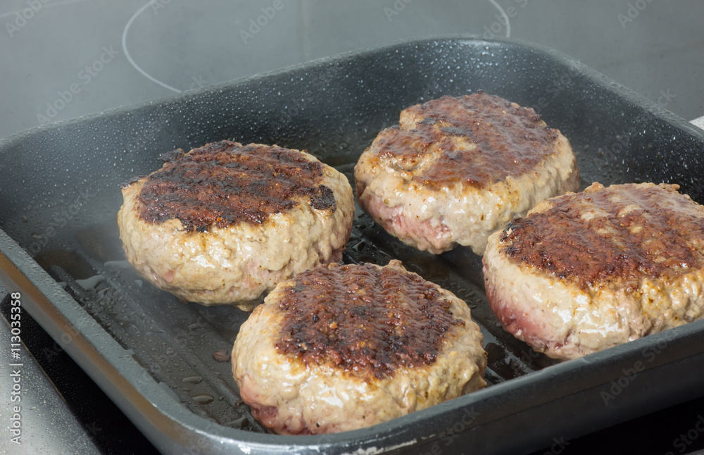 burgers, beef in a frying pan on cooking surface in kitchen burgers, beef in a frying pan on cooking surface in kitchen