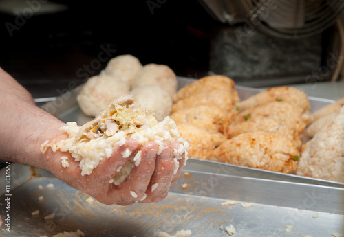 Hand of a cook holding an open typical rice arancino with chicken before modelling it in a cone shape photo