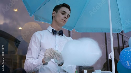 Young guy making cotton candy on a special machine, it wears bow tie, behind him balloons photo