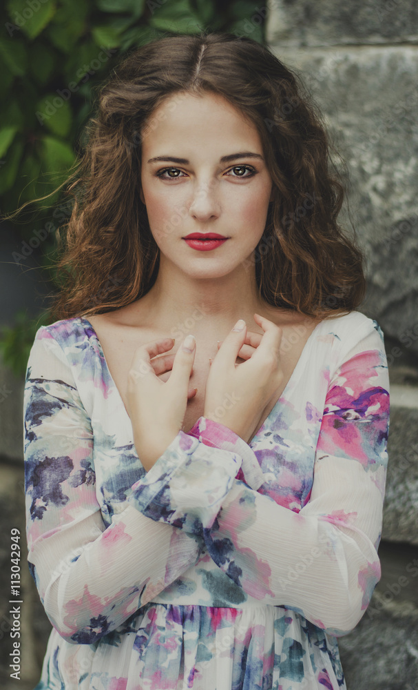 beautiful young woman with brown hair, red lips standing on stone wall background obletennoy branches in white and purple dress beautiful young woman with brown hair, red lips standing on stone wall background obletennoy branches in white and purple dress