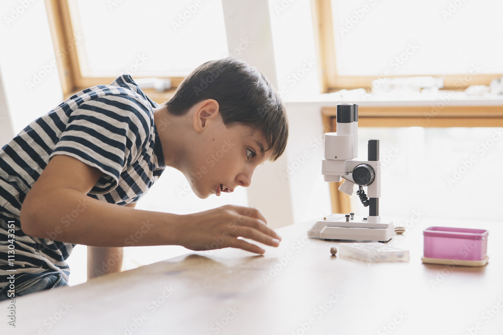 Curious boy looking at microscope on table in house Curious boy looking at microscope on table in house