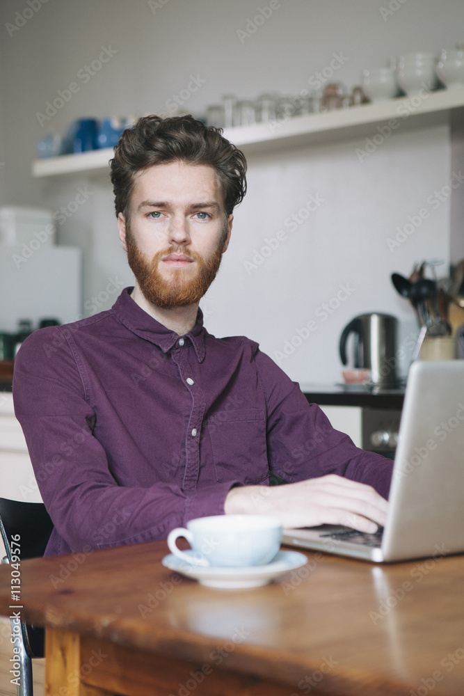 Portrait of confident young man using laptop at table in kitchen Portrait of confident young man using laptop at table in kitchen
