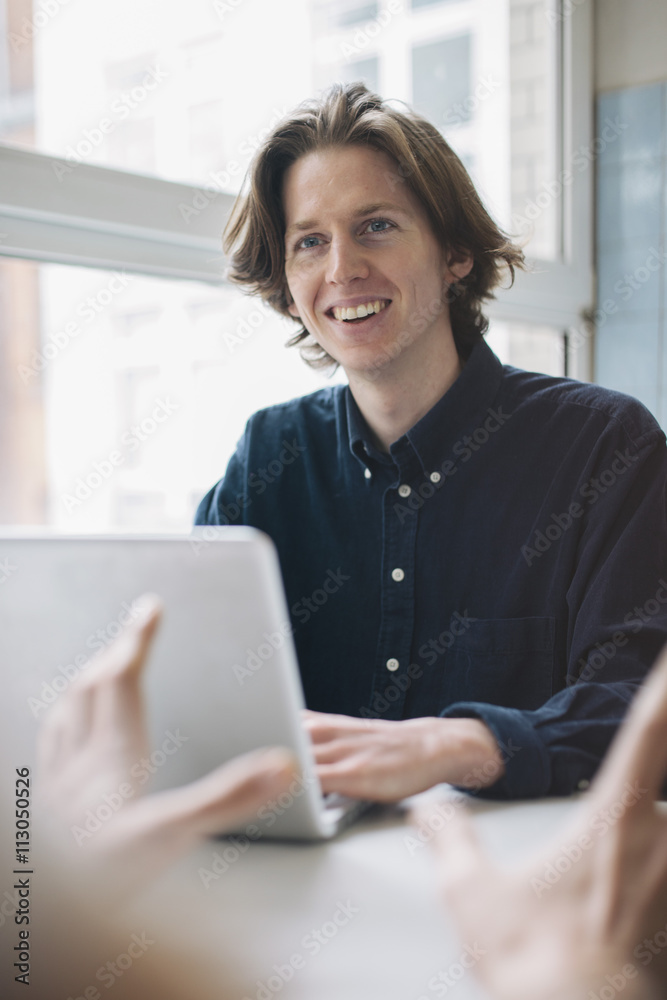 Young man smiling at colleague while using laptop at table