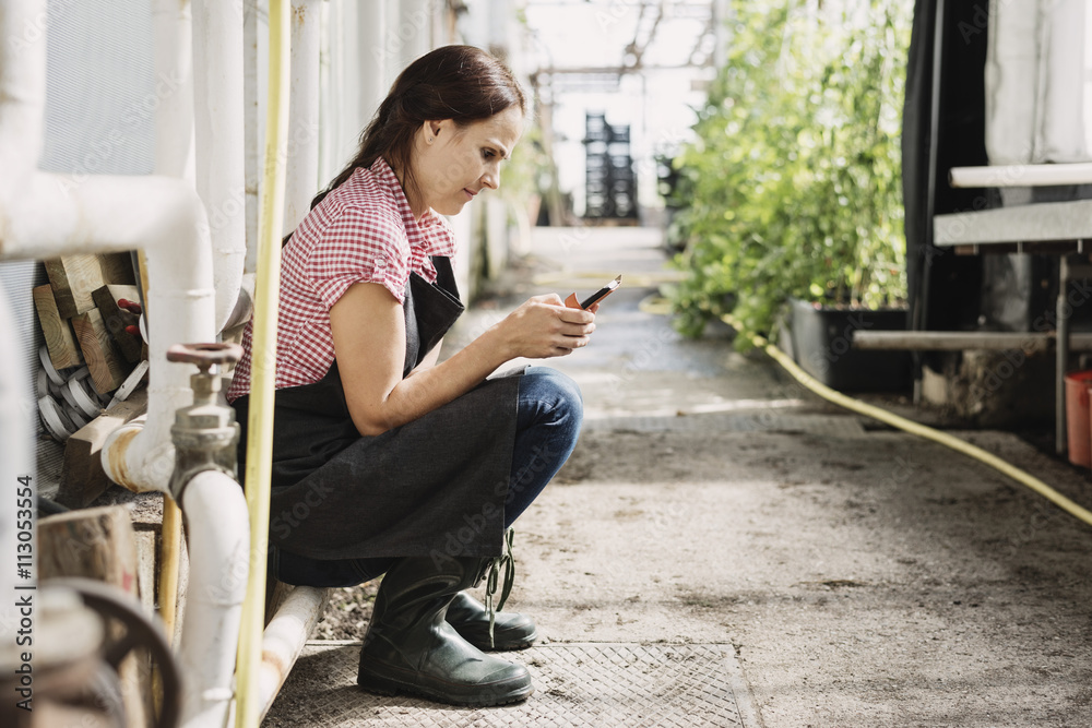 Female gardener text messaging on mobile phone while sitting in greenhouse Female gardener text messaging on mobile phone while sitting in greenhouse