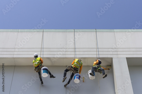 Painters and harnesses hanging high building