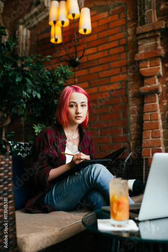 girl working in a cafe using a laptop and notebook