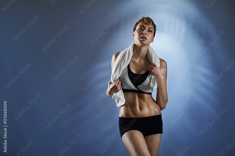 Obraz premium Good training. Shot of a beautiful healthy woman sweating after her workout posing with a towel on blue background copyspace on the side