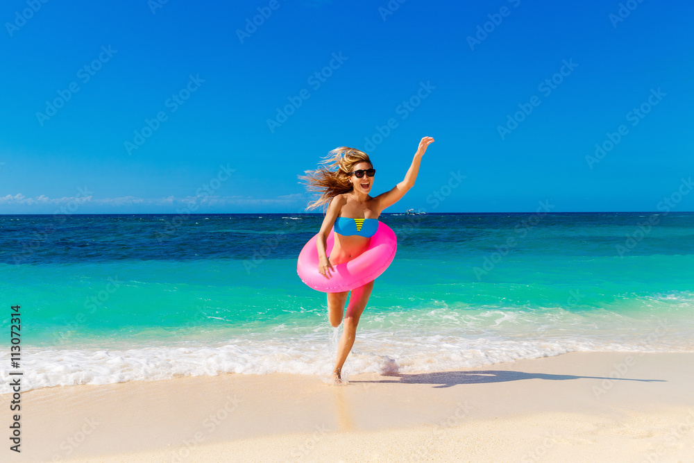 Young happy girl runs out of the tropical sea with rubber ring.