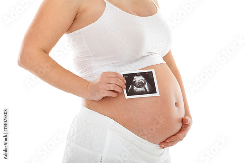 Pregnant woman holding ultrasound scan photo in front of her belly. Isolated on white background. Side view