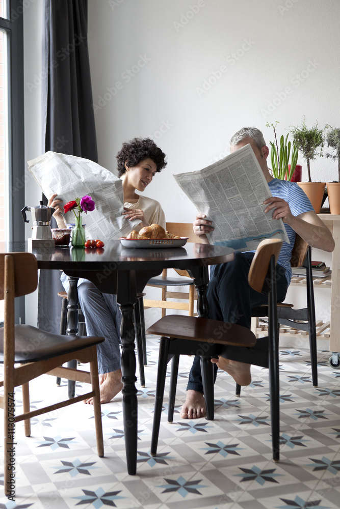 A hip mixed aged couple reading newspapers and having breakfast A hip mixed aged couple reading newspapers and having breakfast