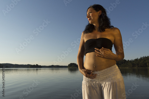 Junge schwangere Yogine beim Mudra am See zur blauen Stunde