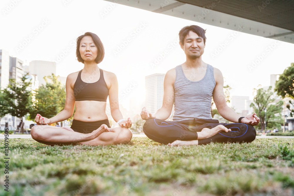 Couple friends doing yoga at sunset on the lawn of the park of the city of Osaka, Japan