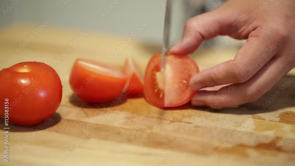 Woman cutting tomato into slides on a wooden board.