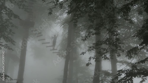 People climbing up the rope ladders in the entertainment park in the forest on a misty or foggy day.  Extreme sports concept.