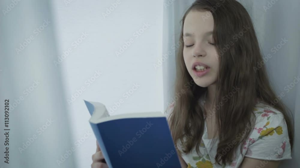 Beautiful little girl reading an interesting book by window. Beautiful little girl reading an interesting book by window.