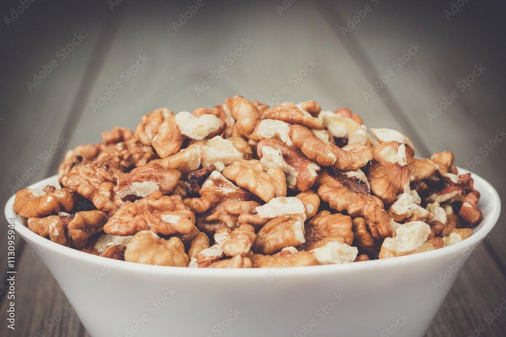 walnuts in the white bowl on brown wooden table walnuts in the white bowl on brown wooden table