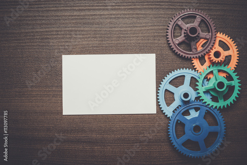 colorful gears and blank notepad on the brown wooden background