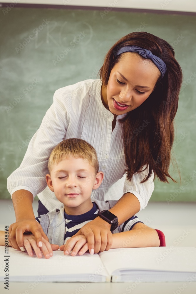 Teacher helping a boy with his homework in classroom Teacher helping a boy with his homework in classroom