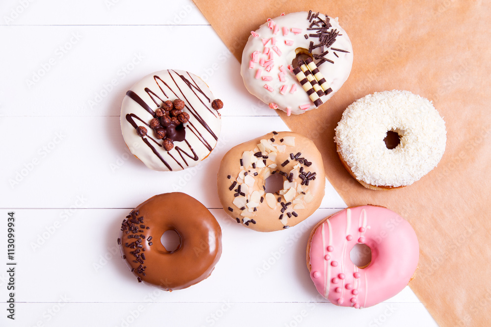 Colored donuts with sprinkles on a white wooden background
