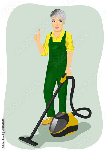 Elderly woman in green coveralls posing with vacuum cleaner and giving thumbs up