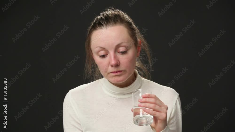 Depression. Sad disheveled woman drinking water from the glass, looking to the camera, black background Depression. Sad disheveled woman drinking water from the glass, looking to the camera, black background