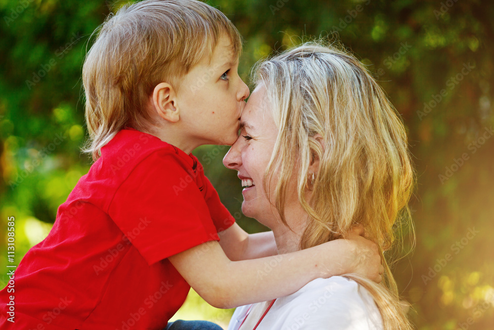 Happy little boy hugging and kissing his mother over green backg Happy little boy hugging and kissing his mother over green backg